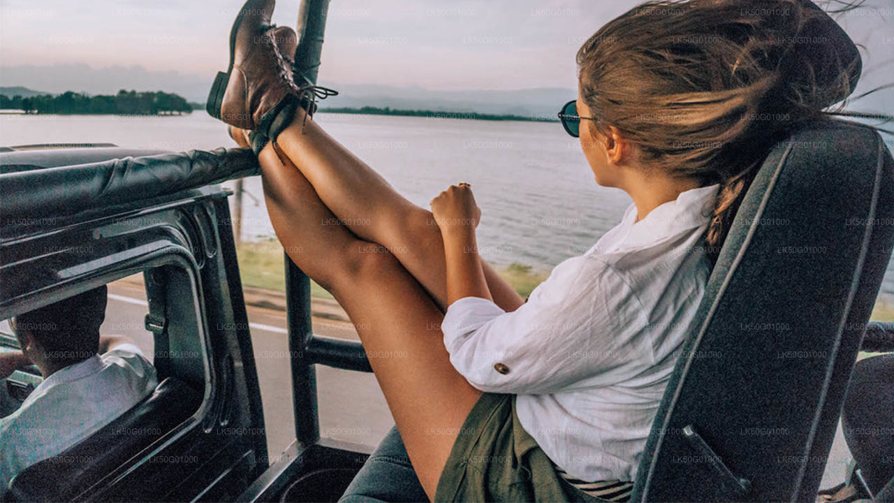 ALT text: Woman relaxing in an open safari jeep with her legs up, wearing boots and sunglasses, enjoying the scenic view of a lake and distant mountains.