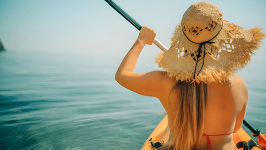 Woman paddling a kayak on a sunny day with clear blue water.
