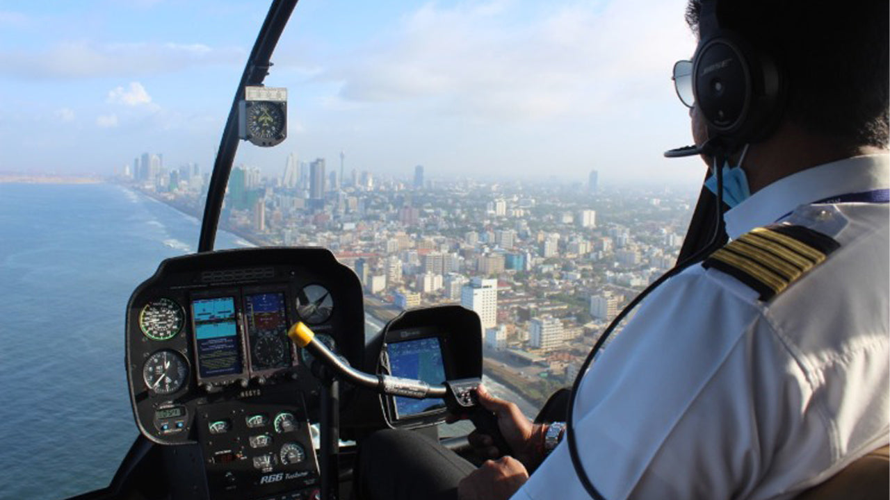 Person piloting a helicopter with a cityscape view from inside the cockpit.